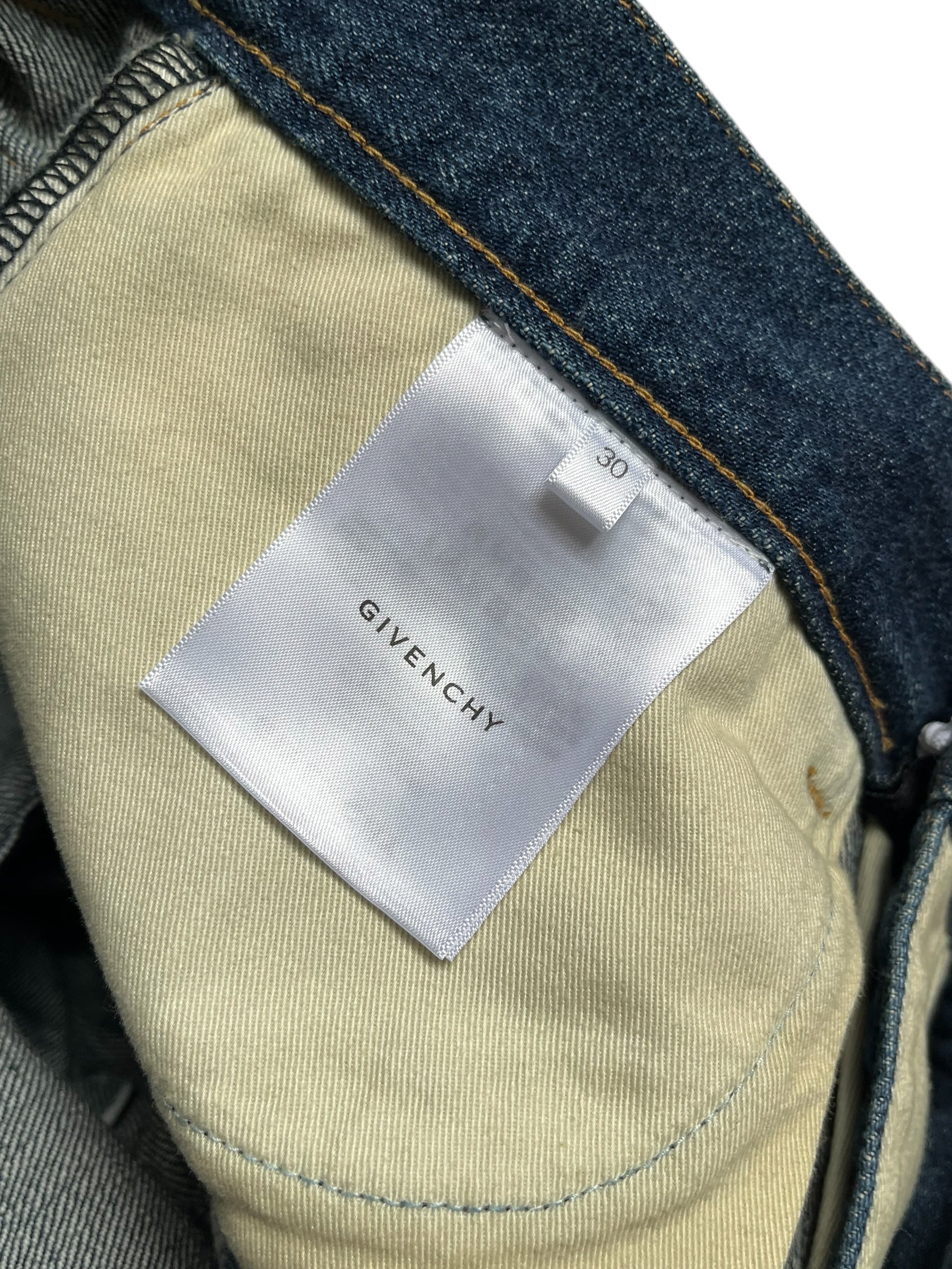 Givenchy FW23 distressed boro blue denim pants with frayed edges and a relaxed fit, displayed on a neutral background.