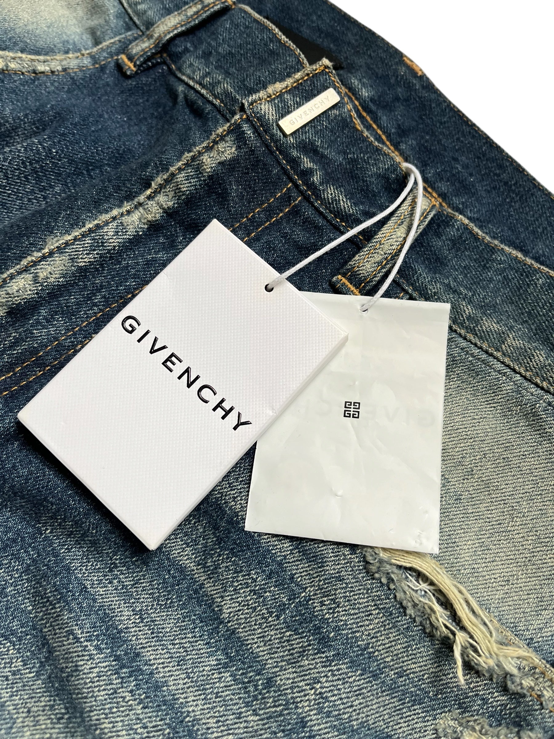 Givenchy FW23 distressed boro blue denim pants with ripped details and a relaxed fit, displayed on a hanger.
