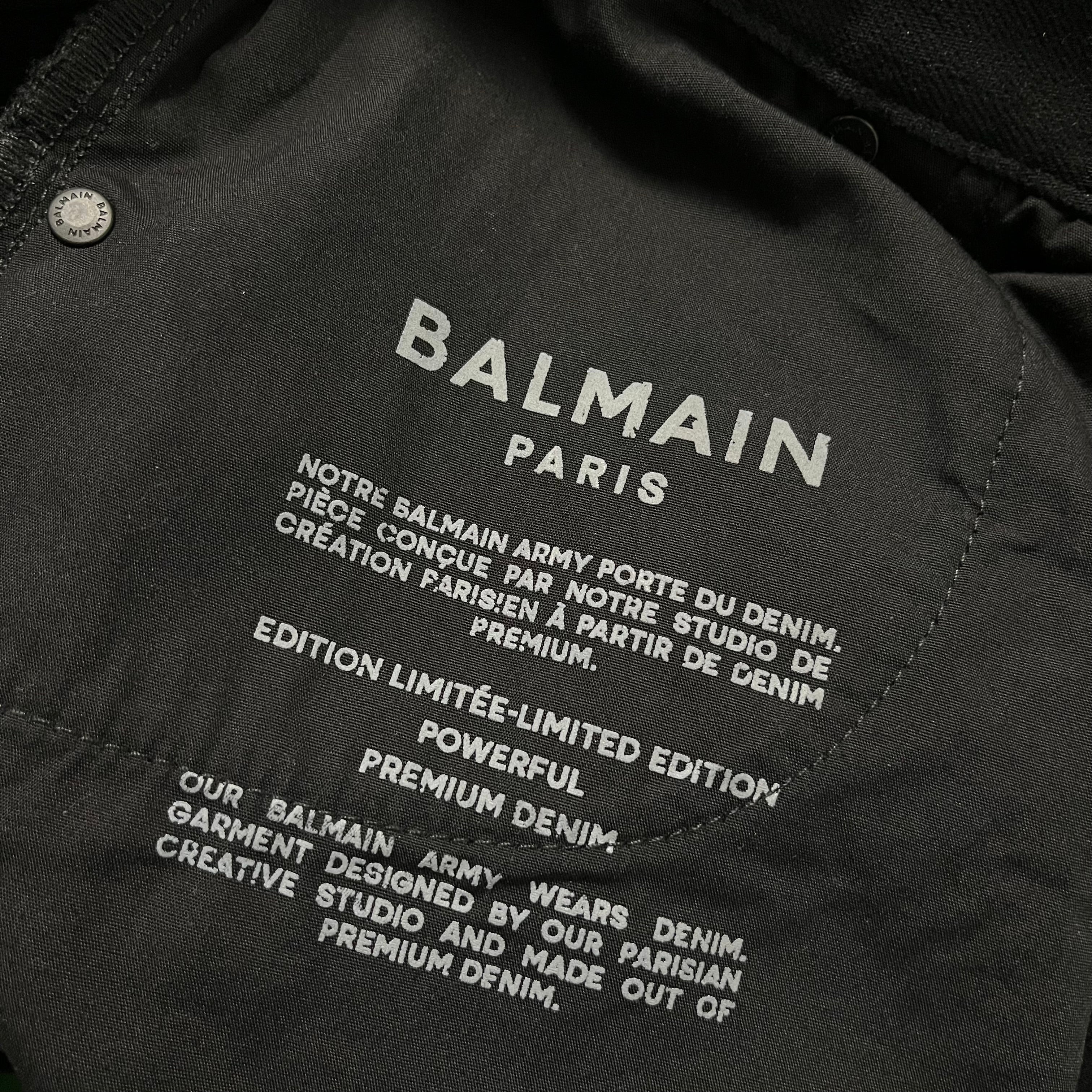 Balmain AW23 limited edition waxed denim pants showing close-up of textured, dark wash fabric with branding details.