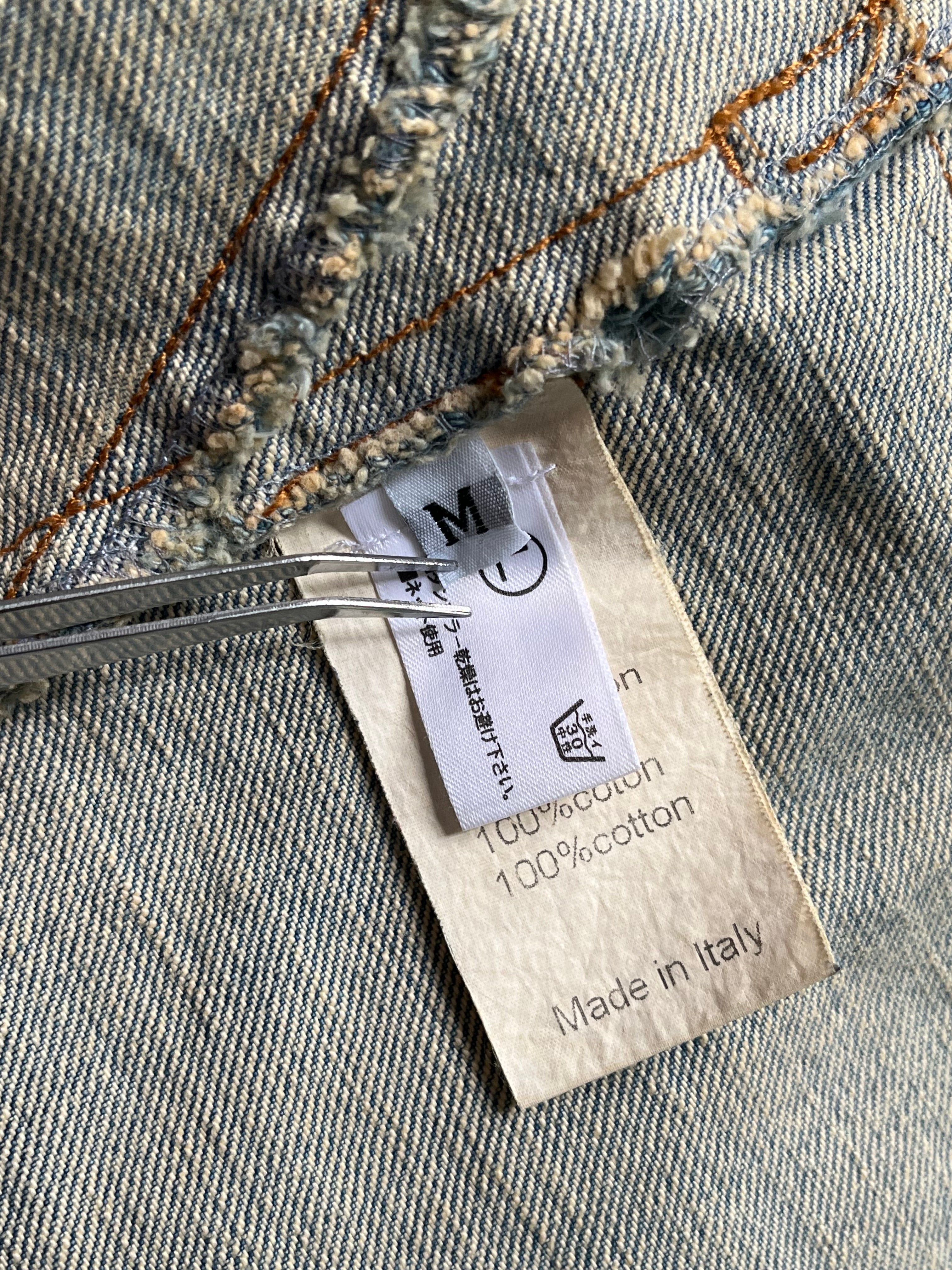 Balmain SS12 G-Dragon Mud Wash Denim Jacket displayed on a hanger, showcasing distressed denim and classic jacket design.