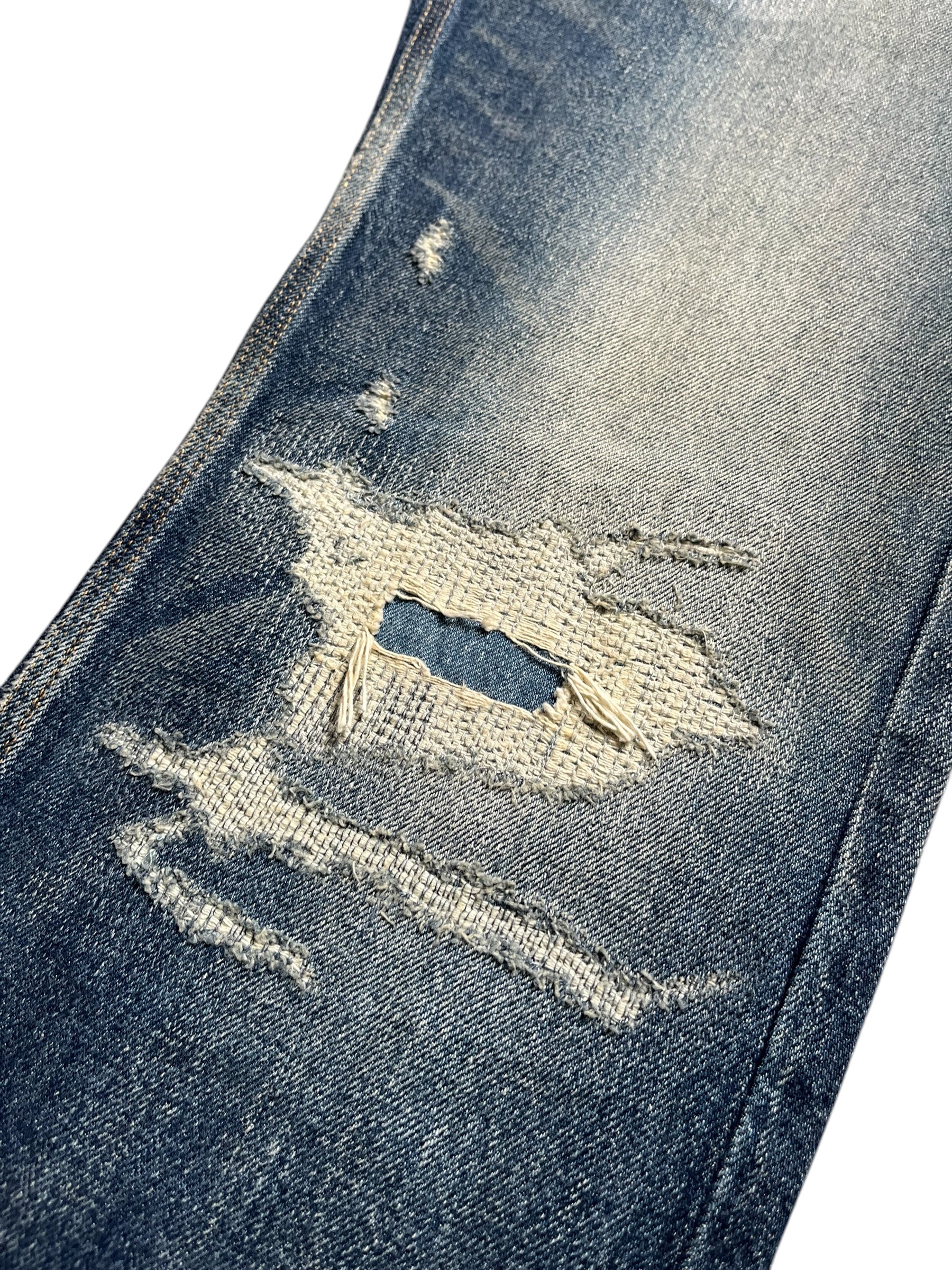 Givenchy FW23 distressed boro blue denim pants, showing a close-up of the ripped and faded denim fabric with branded details.